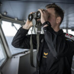 A member of HMCS William Hall conducts lookout duties from the bridge as the ship transits south in the Atlantic Ocean during Operation CARIBBE on 15 May 2025. Photo Credit: Canadian Armed Forces Imagery Technician