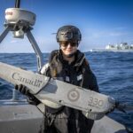 Sailor 3rd Class Paige Timmers poses with His Majesty’s Canadian Ship Ottawa's recovered Puma Drone on route to Korea, for Operation NEON, 7 December 2024. Photo Credit: Sailor 3rd Class Jacob Saunders, Canadian Armed Forces Photo.